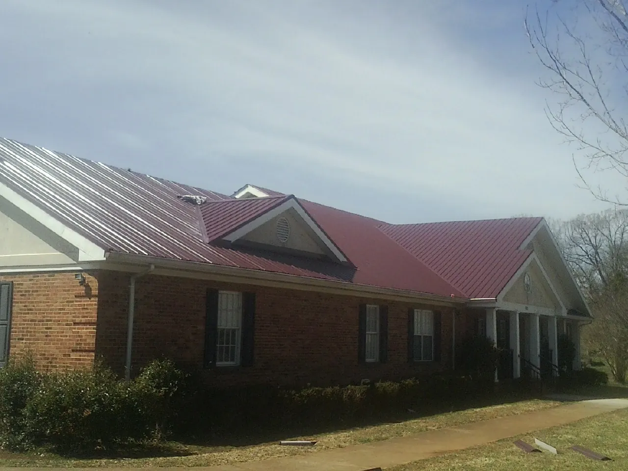 Red metal roof with gabled entries on a long brick building, from a Hail Damage Roof Repair job in Howells